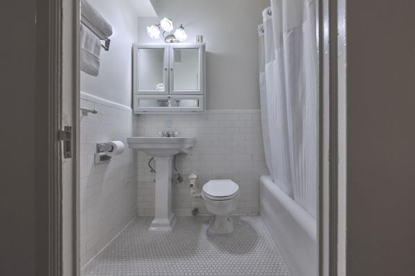 A clean, small bathroom with a pedestal sink, toilet, tub with shower curtain, mirror cabinet, and overhead lights.