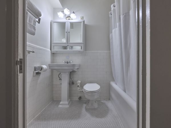 A clean, small bathroom with a pedestal sink, toilet, tub with shower curtain, mirror cabinet, and overhead lights.
