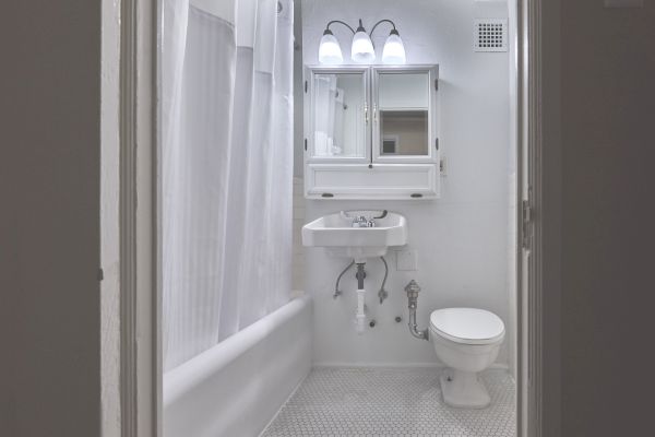 A small, white bathroom with a toilet, sink, mirrored cabinet, and a shower curtain around the bathtub is depicted in the image.