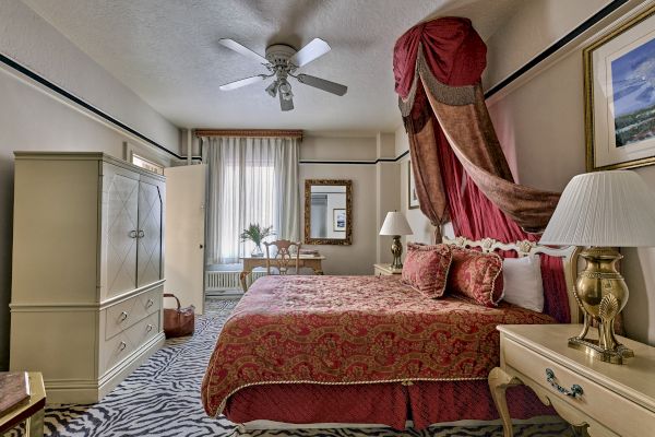 A luxurious bedroom with ornate decor, featuring a draped canopy bed, elegant furniture, and a zebra-patterned rug on the floor.