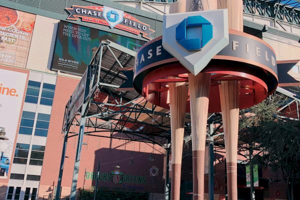 The image shows the entrance to Chase Field with large baseball bats as pillars and a sign above the entrance.