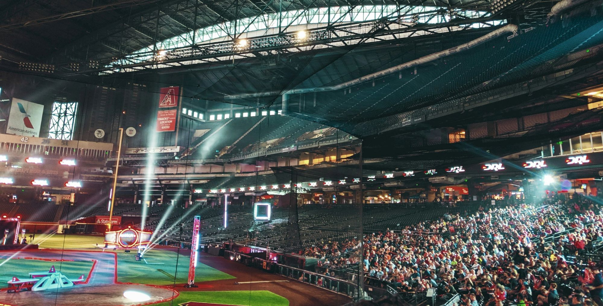 An indoor arena with a large audience, illuminated stage, and colorful lights, possibly hosting a drone racing event.