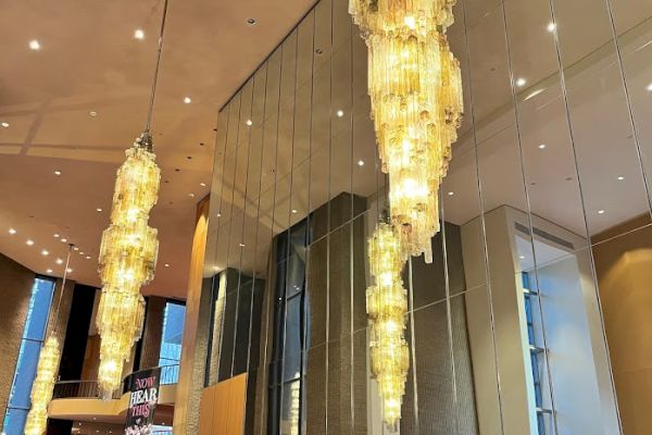 A hotel lobby with large chandeliers, mirrored walls, and people at a reception desk.