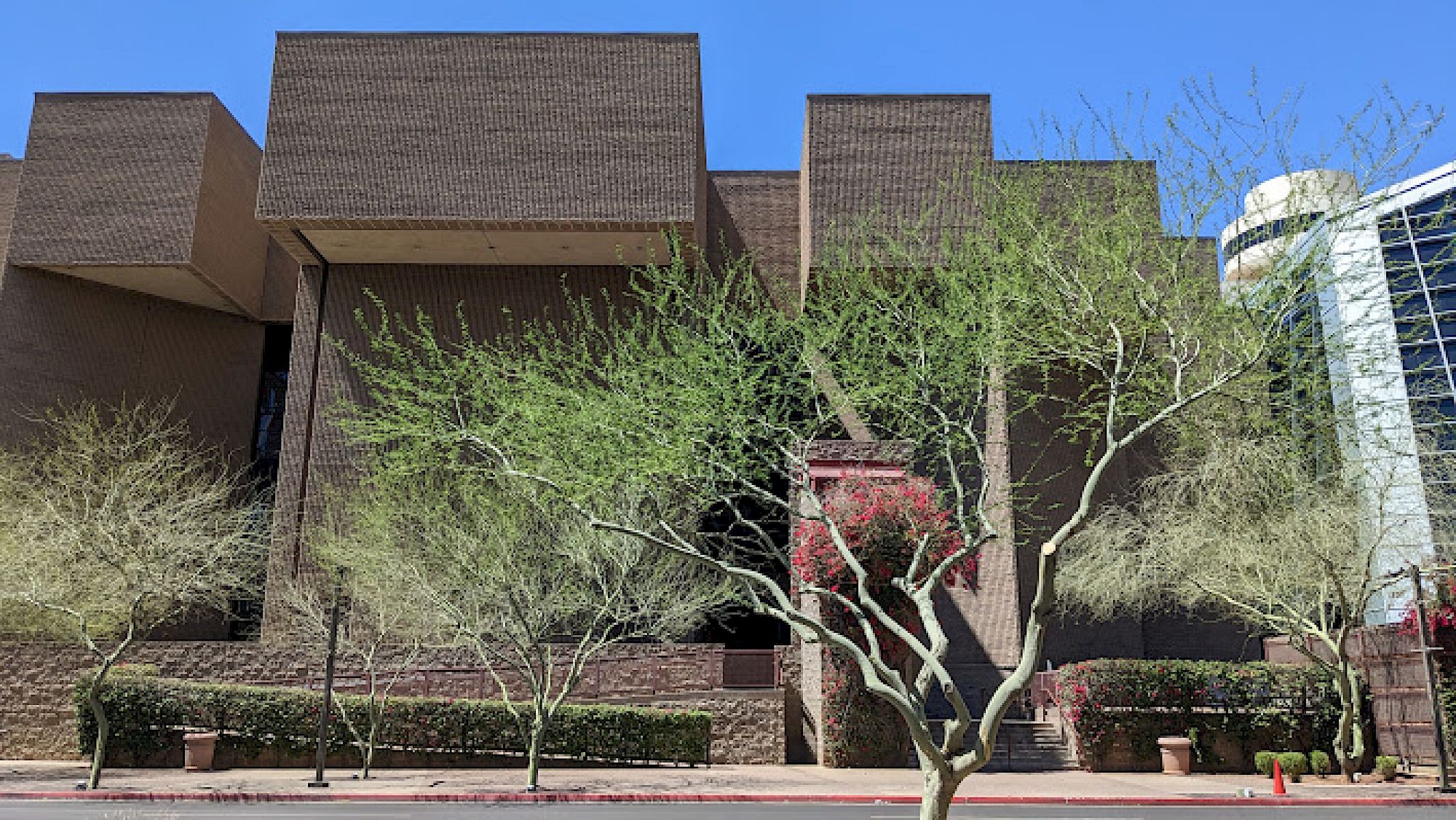 A modern building with a brick facade and cube-like structures, surrounded by leafless trees under a clear blue sky.